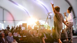 Two women sing on stage on the Harris Theater rooftop, performing to a room full of people.