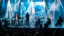 A singer at the forefront of the stage accompanied by an orchestra.