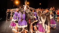 A group of people come together lifting a trophy and celebrating together.