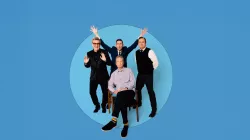 Four older men. One sits on a chair while another stands behind him with his hands in the air. 