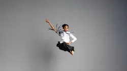 A dancer doing a split in the air and raising her arm up.