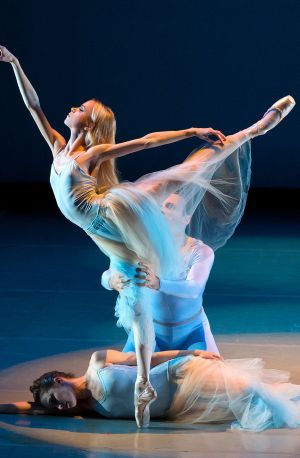 Two female ballerinas in white costumes pose on a softly lit stage