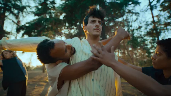 Four dancers in white and grey clothing dance in a wooded setting