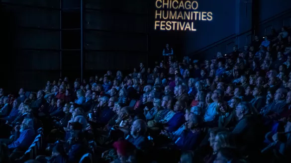 A dark theater filled with people, with Chicago Humanities Festival projected against the wall in white letters