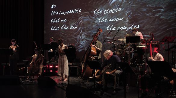 An ensemble of musicians perform in front of projected drawings and text