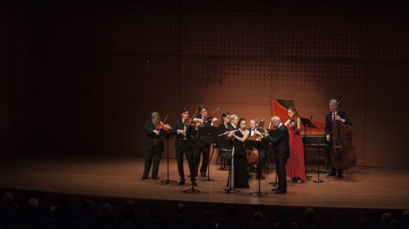 Several CMS musicians under a spotlight  wearing black and red outfits, playing intruments 