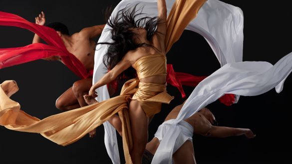 Three dancers wear red, gold, and white sashes around their bodies.