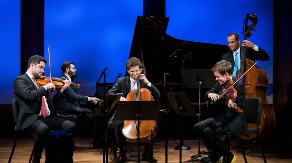 Five musicians playing on stage smiling. 