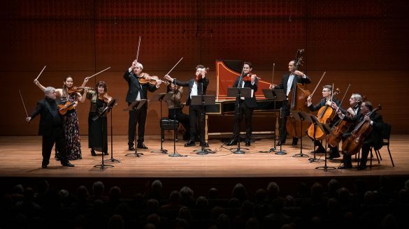 An ensemble of musicians on stage lifting their bow's as if they are finished playing.