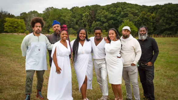 A group of people pose together outside in a park and forest.