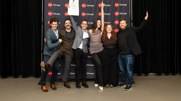 Six people celebrating their award at AIA Chicago's Designight, posing together in front of a backdrop with repeated AIA Chicago logos. Two people in the center are holding up certificates or awards while the group strikes jubilant poses with raised arms and big smiles."