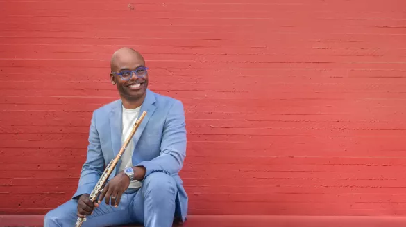Demarre McGill sits against an orange background holding his flute.