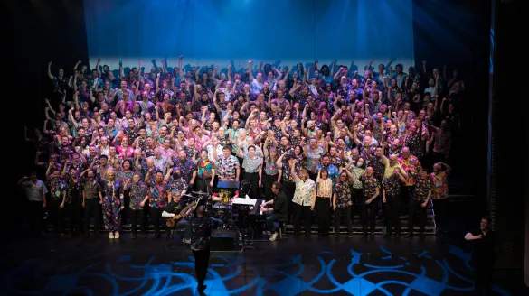 A large chorus of men singing on the Harris stage. 