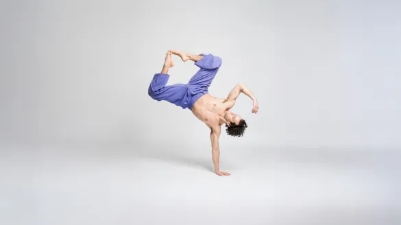 A dancer on stands on one arm with his legs come together. 