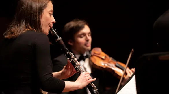 A woman playing the clarinet while a man plays the violin
