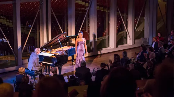 J'Nai Bridges performing in front of an audience while Craig Terry plays the piano.