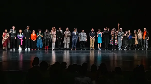 2025 3Arts Awardees standing in a curtain call line on the Harris Theater stage, waving and smiling at the audience.