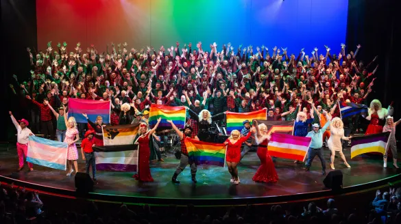 A large chorus holding LGBTQIA+ flags