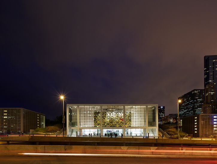 Image of the white concrete and glass facade of the Harris Theater, against a dark purple and gray night sky