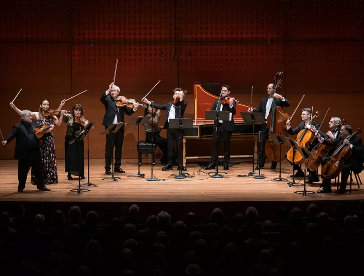 An ensemble of musicians on stage lifting their bow's as if they are finished playing.