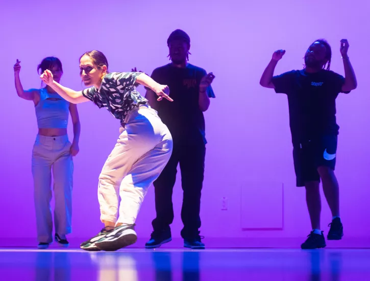 Dancer smiling and performing with three other dancers in the background.