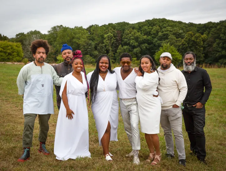 A group of people pose together outside in a park and forest.