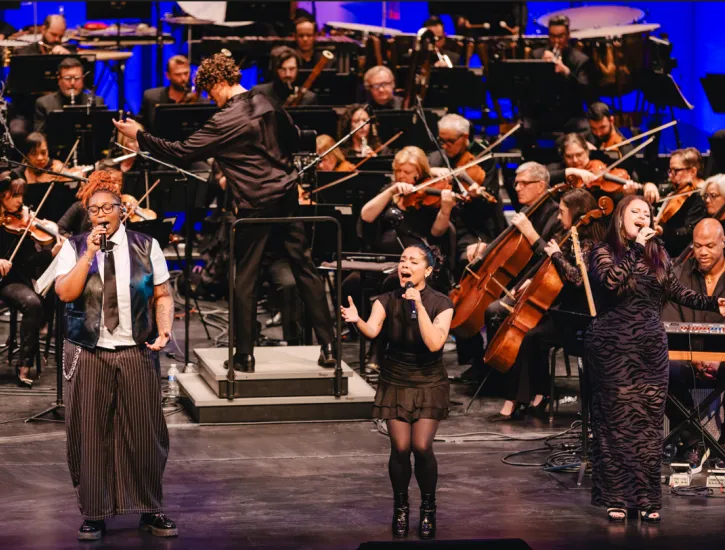 Three vocalists singing while Steve Hackman conducts the Chicago Philharmonic.