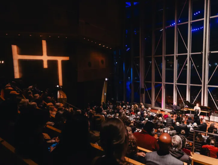 An audience looking at three artists perform on the Pritzker Pavilion stage looking toward the city of Chicago during the nightime. 