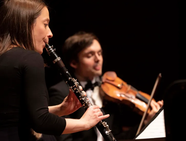 A woman playing the clarinet while a man plays the violin