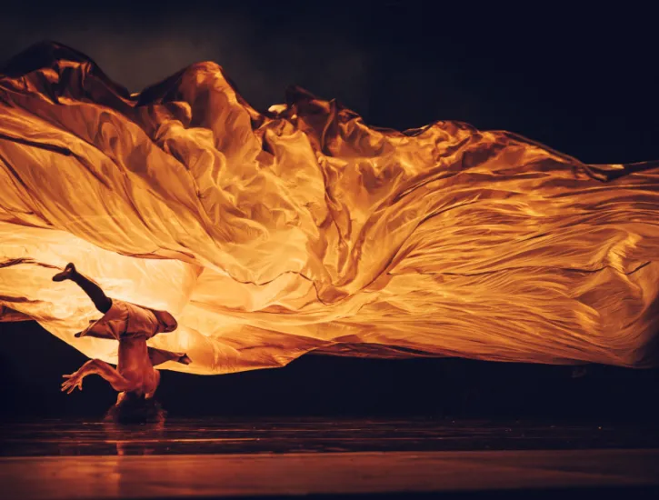 A dancer upside down while a drape flows over him. 