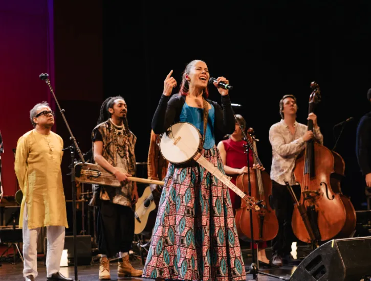 Rhiannon Giddens singing while the ensemble stand behind her with their instruments. 