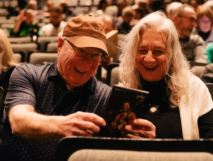 Two patrons smiling and reading the program book while seated in the Harris Theater auditoriunm.